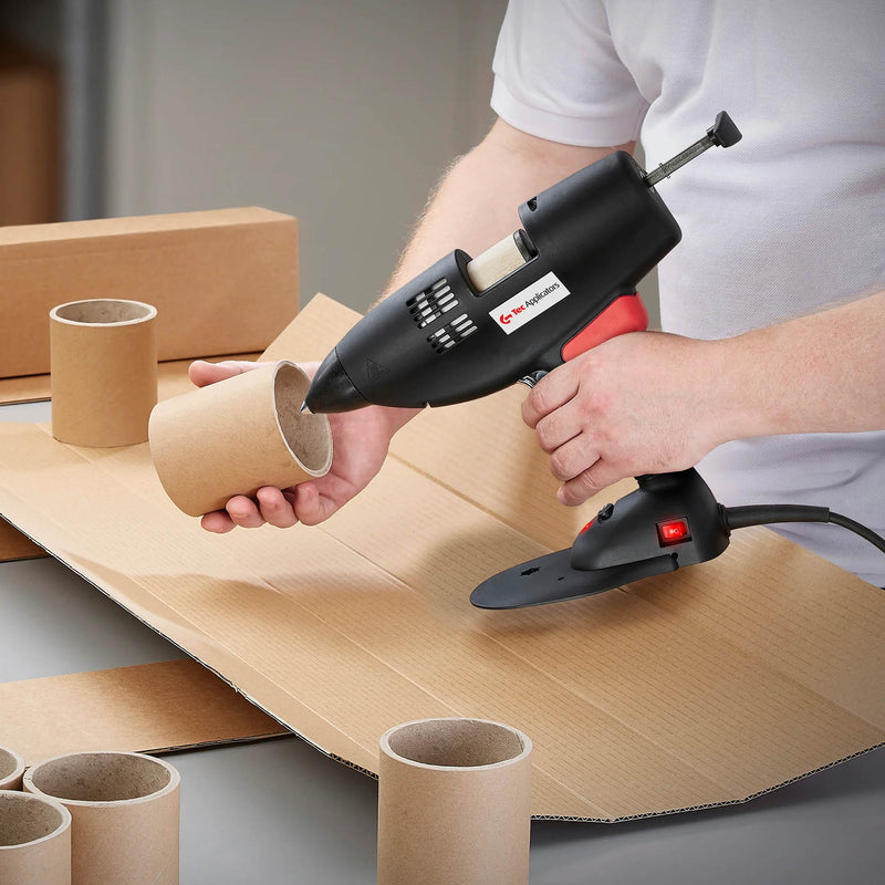 Worker applying glue to a cardboard cylinder using a hot glue gun